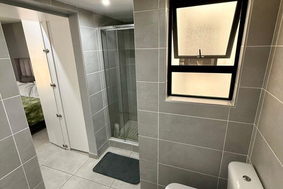 A modern bathroom featuring grey floor-to-ceiling tiles, a glass-enclosed shower, a white toilet, and a wall-mounted basin.