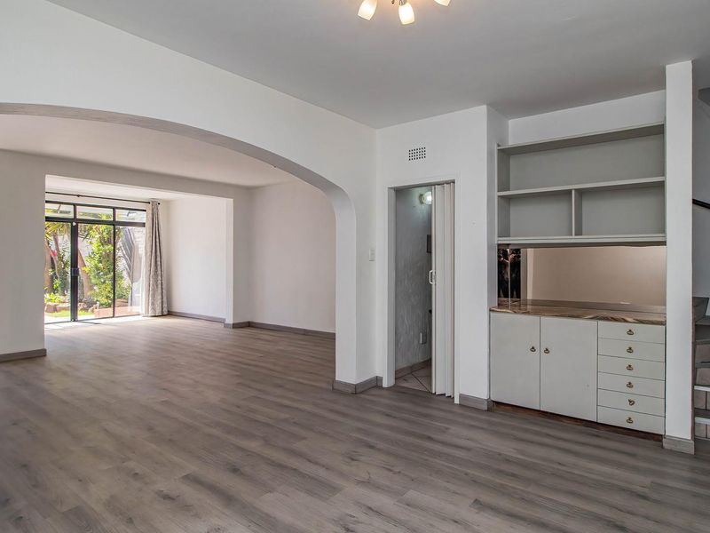 Spacious open-plan living area featuring laminate flooring, a built-in storage unit, an elegant archway, and direct access to the garden through sliding glass doors.