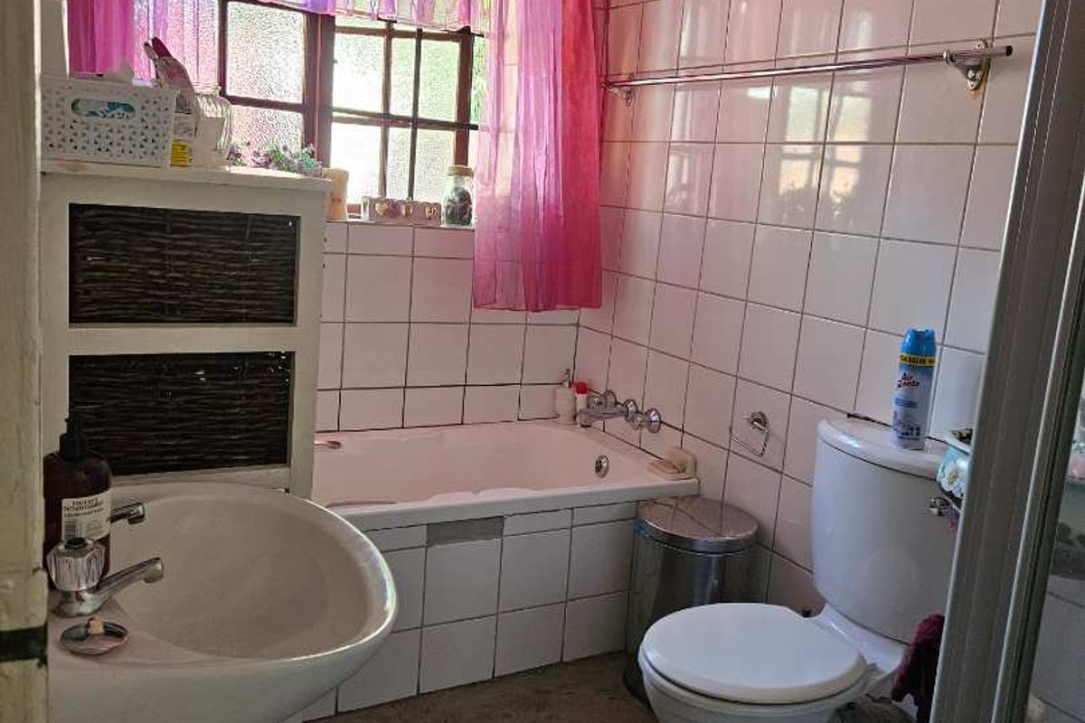 A dated bathroom featuring a built-in bathtub, pedestal sink, and toilet, with wall-to-wall tiling and a window for natural light.