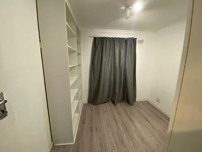A clean, empty bedroom featuring modern laminate flooring, a built-in shelving unit, and neutral walls, ready for personalization.
