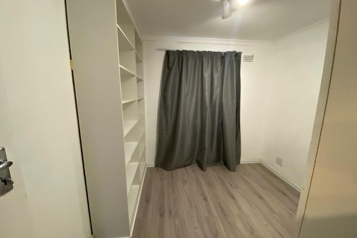 A clean, empty bedroom featuring modern laminate flooring, a built-in shelving unit, and neutral walls, ready for personalization.