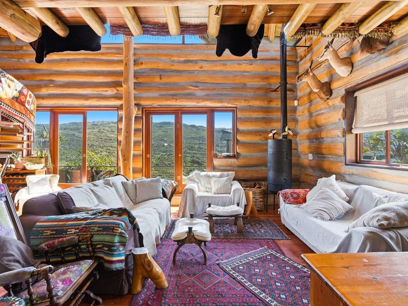 Rustic living room featuring exposed log walls, timber beam ceilings, a wood-burning stove, and large glass doors offering scenic mountain views.