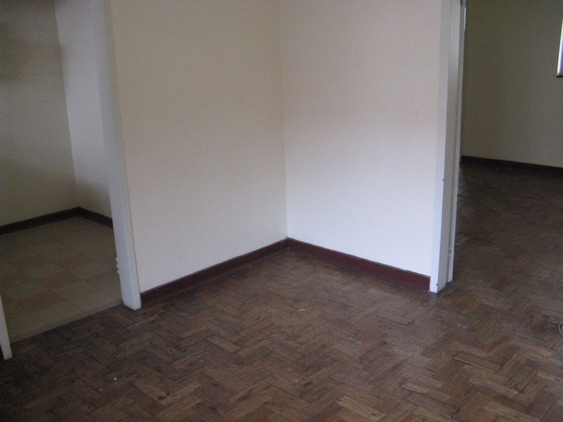 An empty living area featuring traditional parquet flooring and neutral walls, offering a blank canvas for renovation or interior design updates.