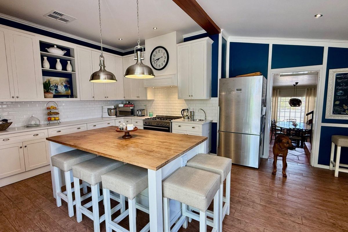A well-appointed kitchen featuring white cabinetry, a central wooden island, subway tile backsplash, and integrated stainless steel appliances.