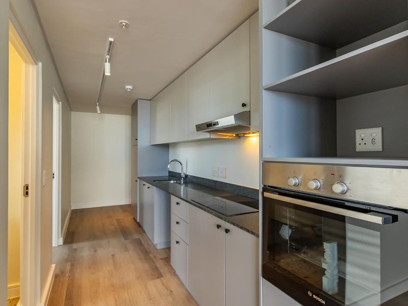 Modern galley-style kitchen featuring sleek cabinetry, stone countertops, integrated oven, hob, and extractor fan with contemporary track lighting.