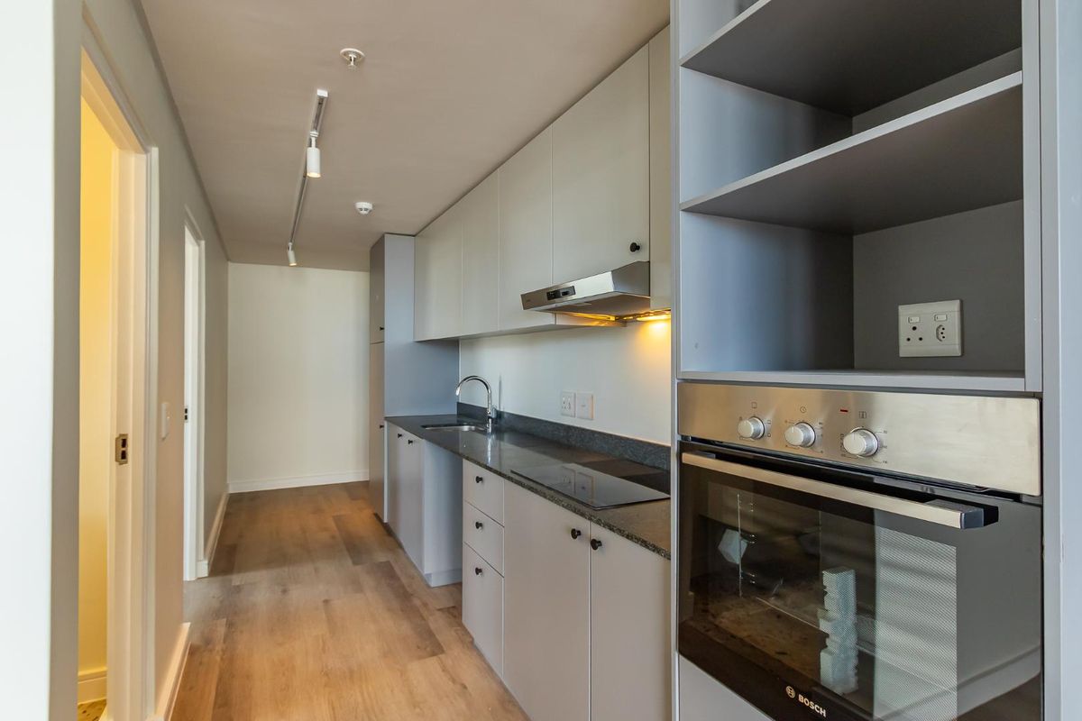 Modern galley-style kitchen featuring sleek cabinetry, stone countertops, integrated oven, hob, and extractor fan with contemporary track lighting.