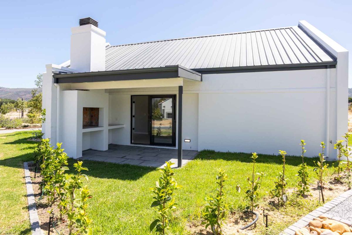 A well-maintained rear exterior view featuring a covered patio with a built-in braai, metal roof, and landscaped garden area.