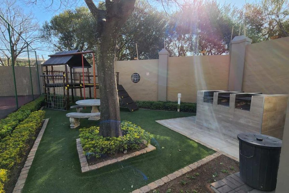 A well-maintained rear garden area featuring a built-in braai, paved patio space, and artificial lawn, perfect for outdoor entertaining.