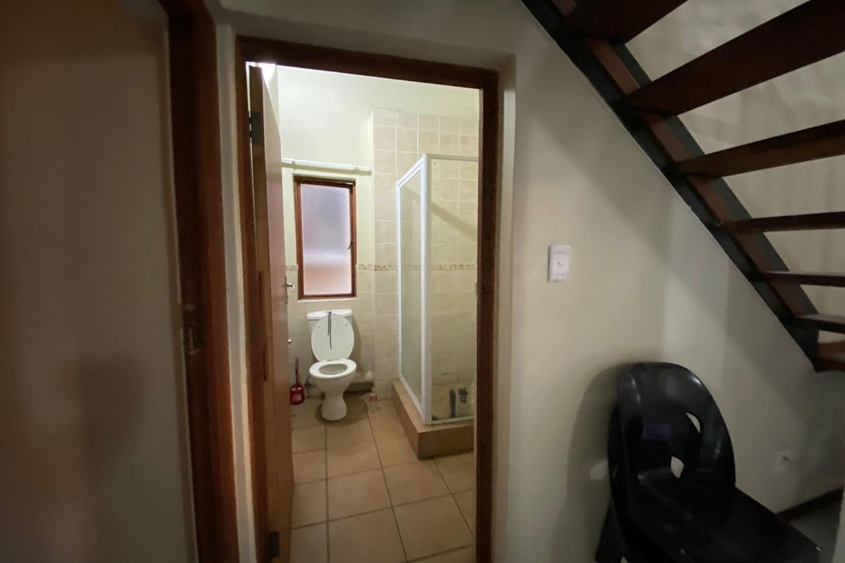 A functional bathroom featuring a shower enclosure, toilet, and tiled flooring, conveniently located under the staircase.
