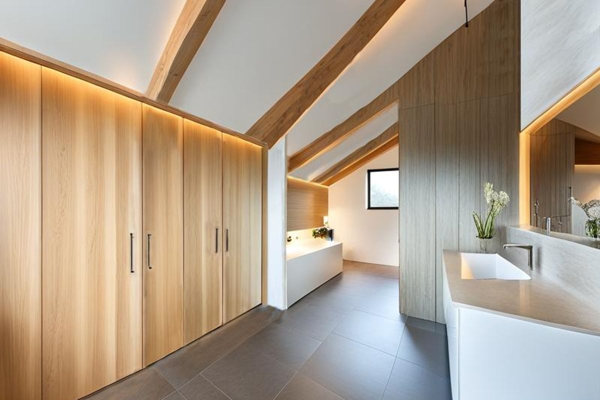 Modern luxury bathroom featuring exposed timber beams, extensive built-in cabinetry, integrated LED lighting, a sleek vanity basin, and a freestanding bathtub.