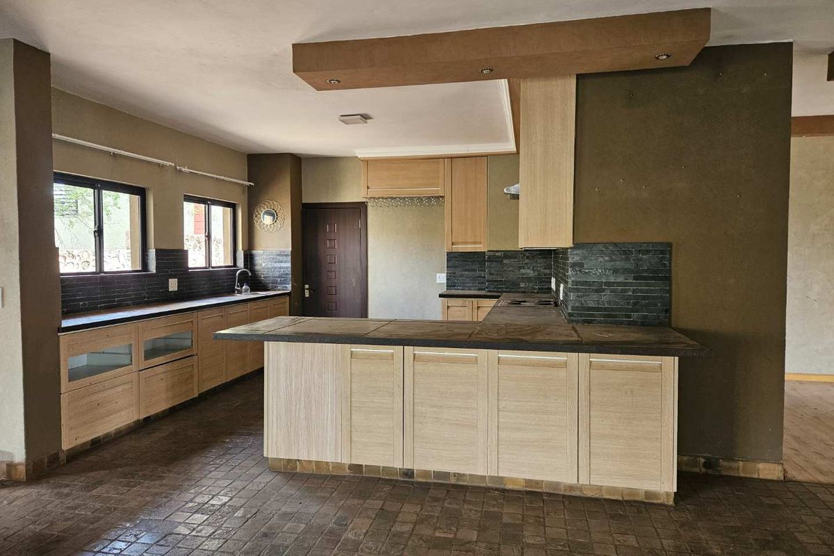 Spacious kitchen featuring light wood cabinetry, stone countertops, a central island, and a dark stone tile backsplash with integrated lighting.
