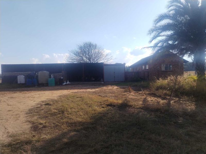 Rear view of the farm property featuring a brick outbuilding with metal roofing and storage tanks set on an unpaved yard.