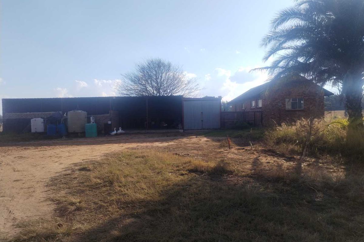 Rear view of the farm property featuring a brick outbuilding with metal roofing and storage tanks set on an unpaved yard.