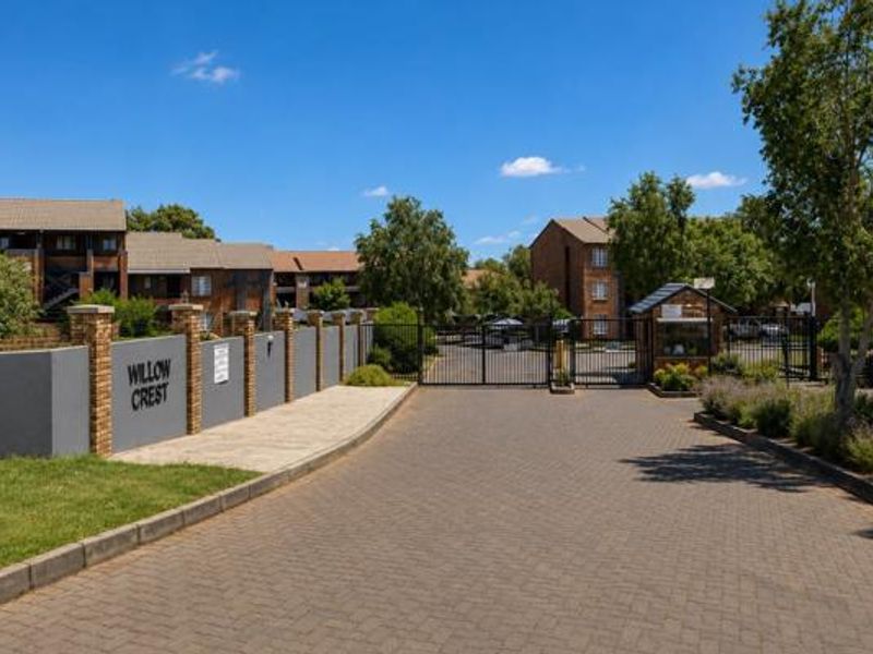 The entrance to Willow Crest apartment complex featuring a paved driveway, secure gated access, and a dedicated guard house.