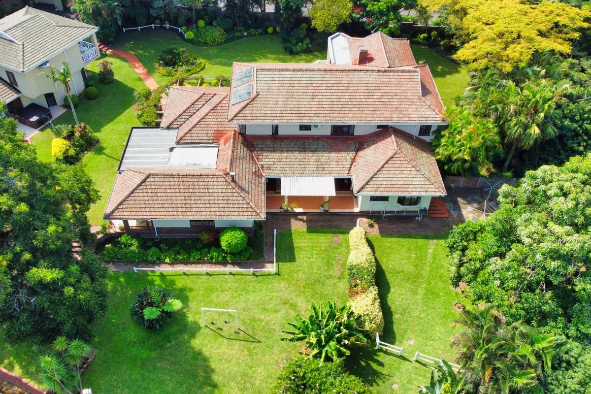 Aerial view of a large residential property featuring a multi-pitched tiled roof, expansive green lawns, mature trees, and a covered patio area.