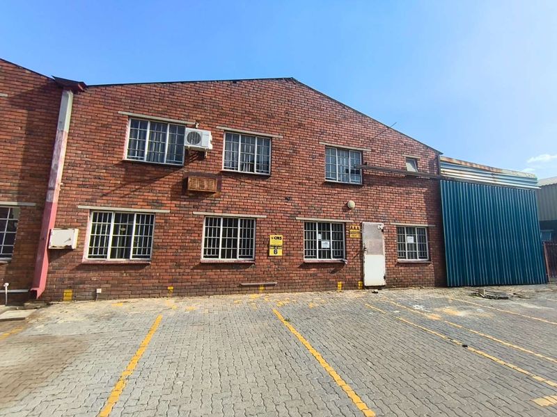 Front elevation of an industrial brick building featuring steel-framed windows, wall-mounted air conditioning units, and a dedicated paved parking area.
