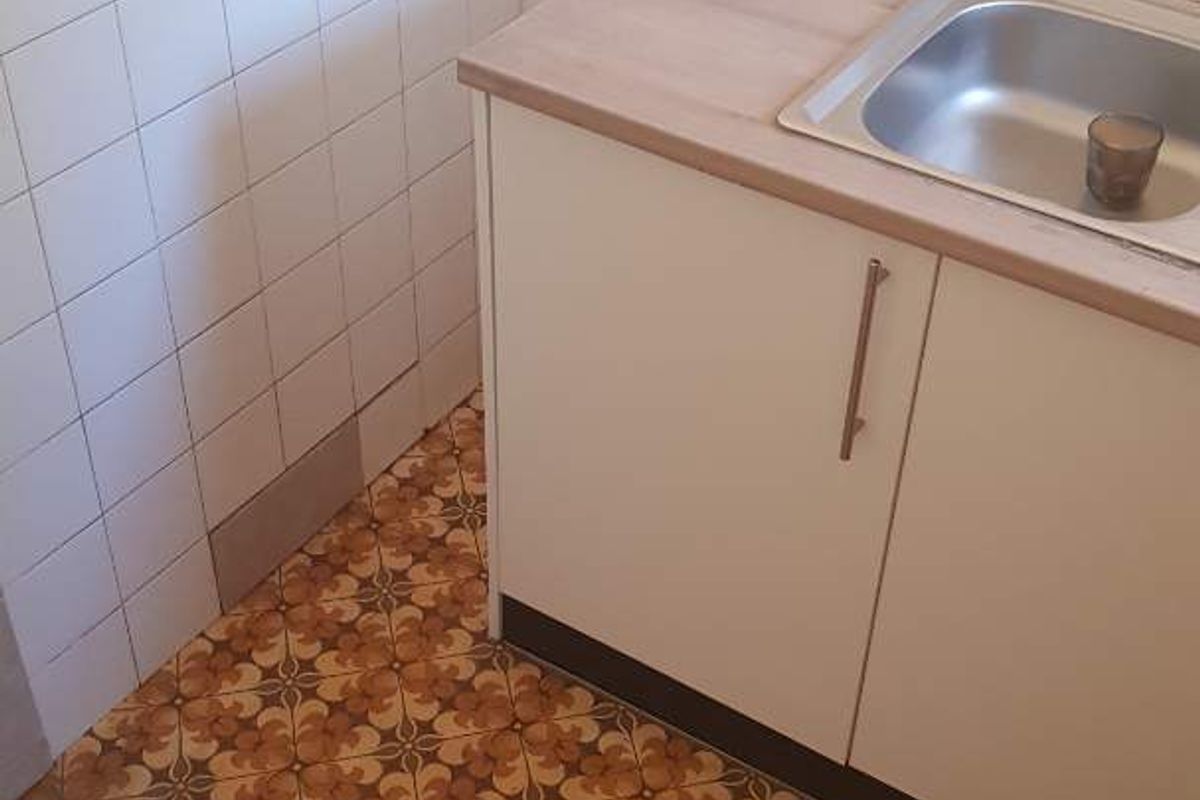 A small kitchen area featuring a stainless steel sink, base cabinetry, and tiled splashback, currently requiring flooring repairs.