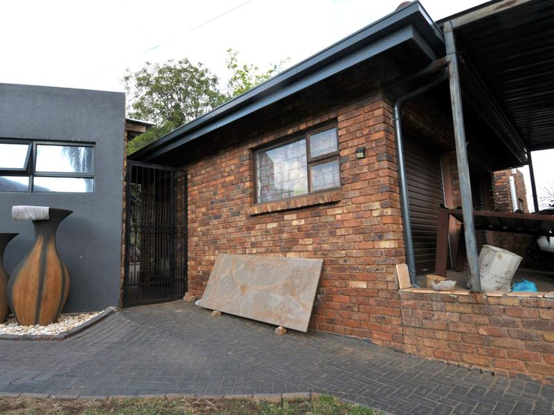 Front exterior view of a face brick townhouse featuring a paved driveway, metal security gate, and a covered carport area.