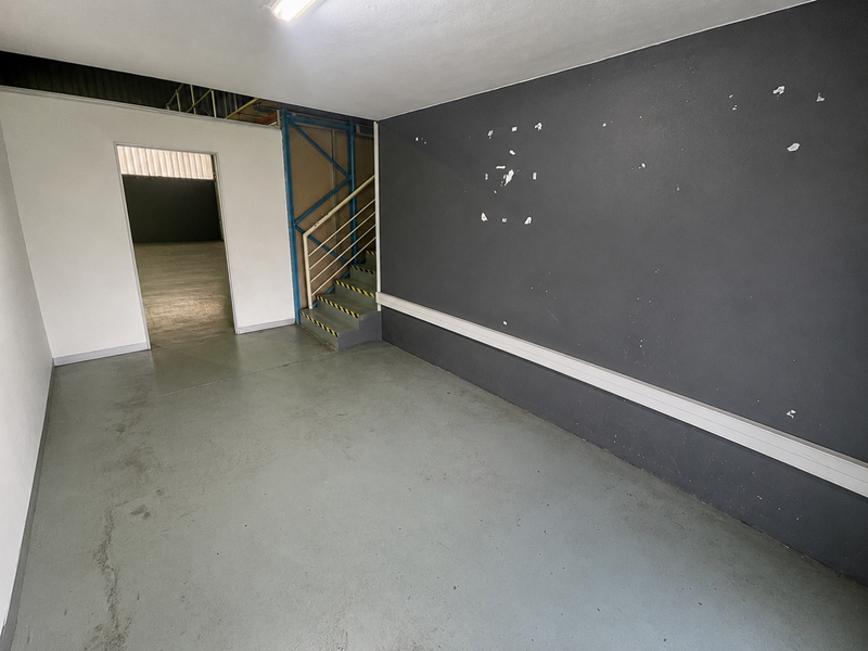 An empty utility or industrial space featuring concrete flooring, a metal staircase, and dark accent walling, suitable for various commercial or storage applications.