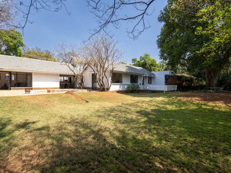 A view of the rear elevation of the house featuring a paved patio area and a spacious garden with mature trees.