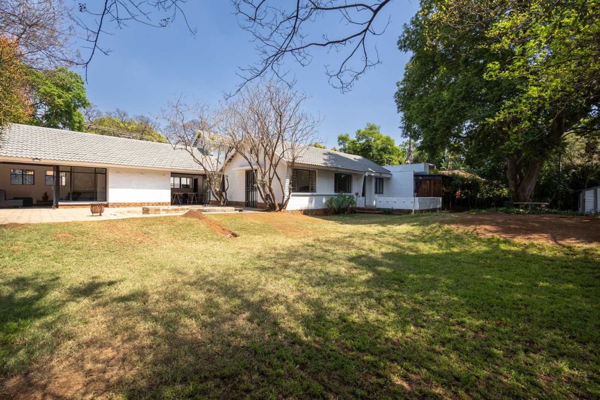 A view of the rear elevation of the house featuring a paved patio area and a spacious garden with mature trees.