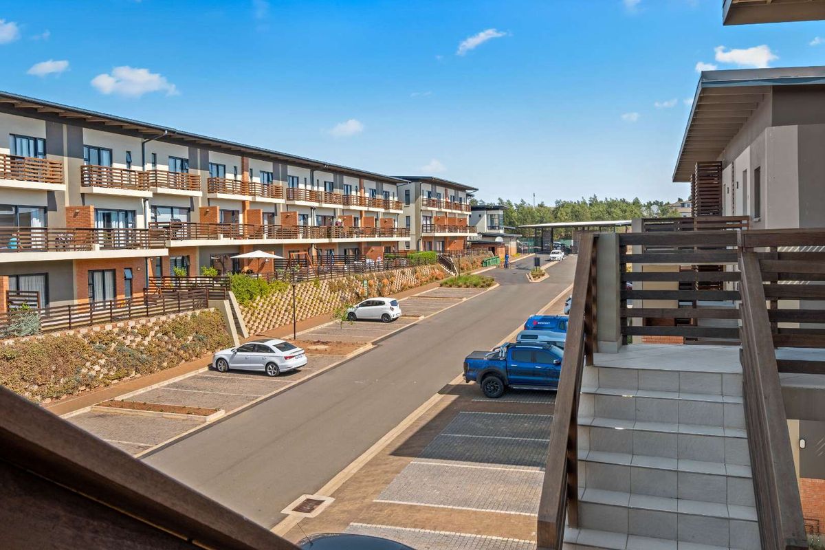 An elevated view of the apartment complex exterior, featuring paved parking bays, a retaining wall, and access staircases between the residential blocks.