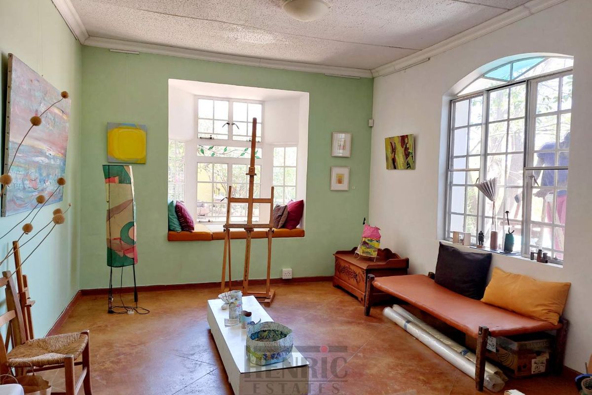 A bright living room featuring large arched windows, a built-in window seat, and terracotta-style flooring, offering a versatile space with natural light.
