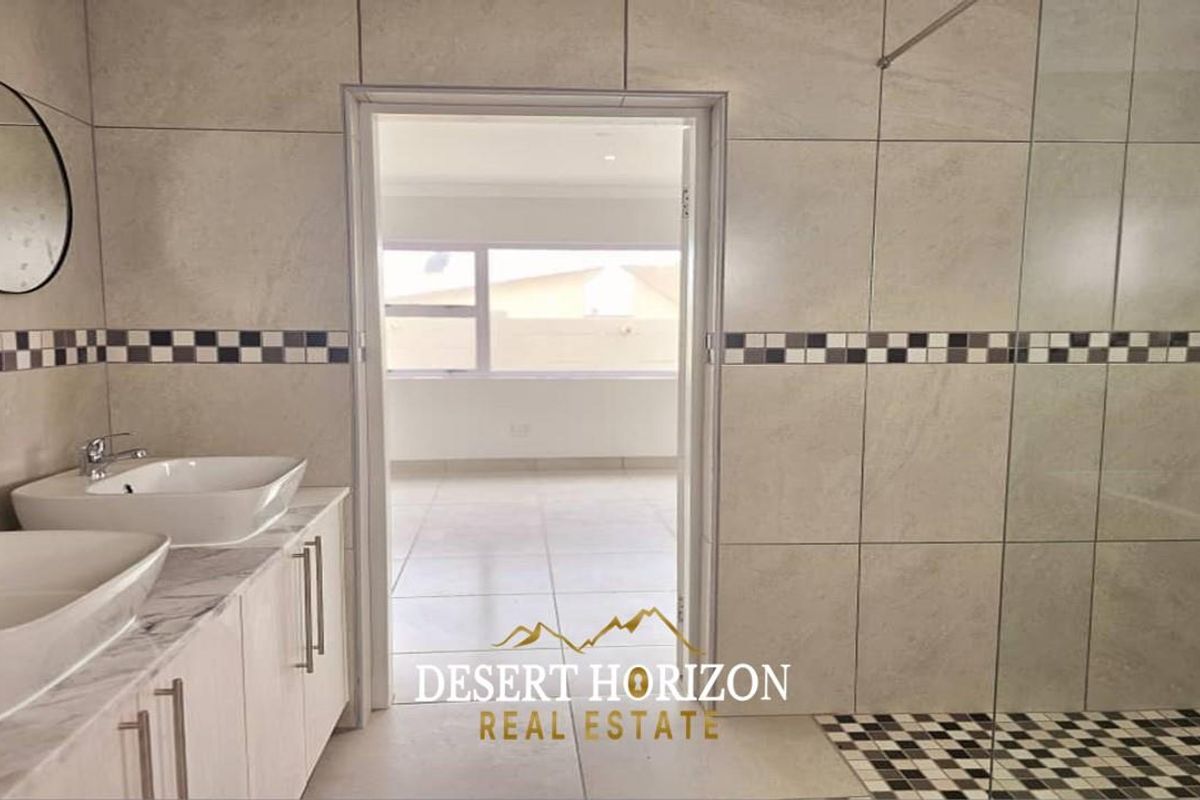 Modern bathroom featuring dual vessel sinks on a vanity, a glass-enclosed shower with tiled walls, and a doorway leading to an adjacent room.