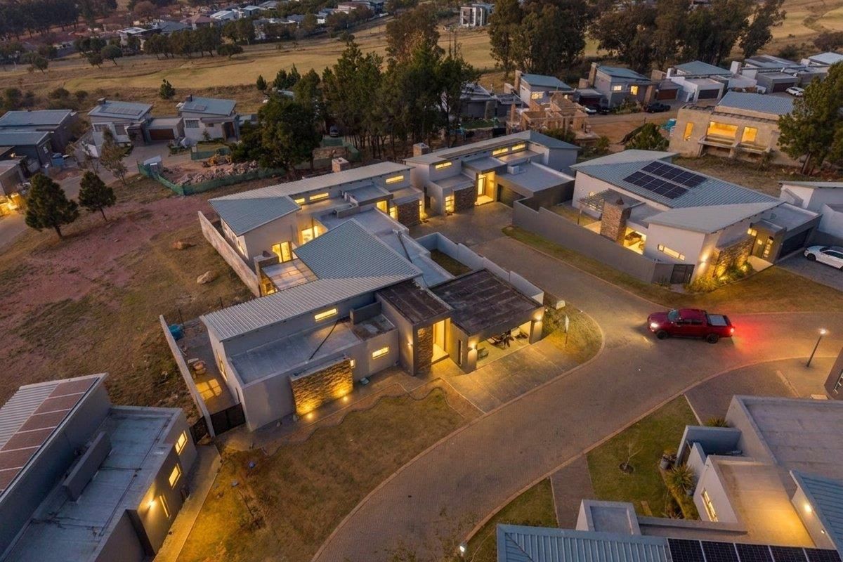 Aerial view of a modern residential property featuring contemporary architecture, stone accents, metal roofing, solar panels, and a paved driveway in a suburban estate.