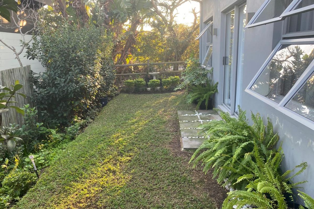 A well-maintained rear garden featuring a manicured lawn, concrete stepping stones, and modern awning windows providing access to the home.