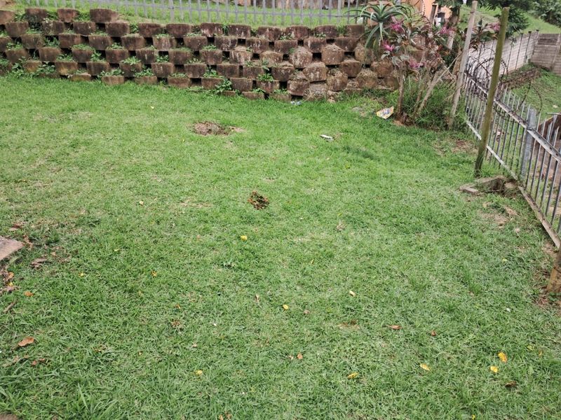 A private garden area featuring a grass lawn, a tiered concrete block retaining wall, and metal perimeter fencing.
