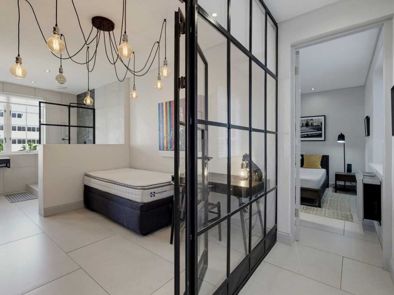 Modern bedroom featuring a stylish industrial steel and glass partition, tiled flooring, and an integrated en-suite bathroom area with contemporary finishes.