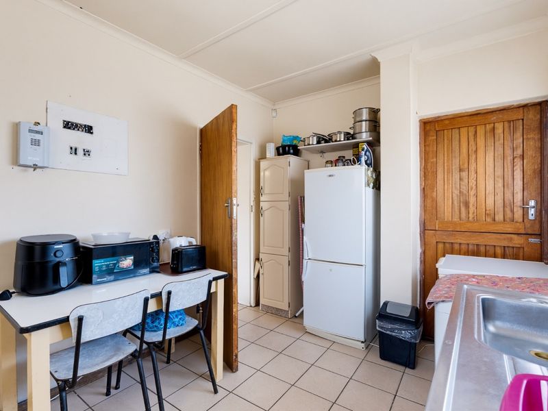 A functional scullery area featuring tiled flooring, a stainless steel sink, and built-in storage cabinetry, providing practical utility space for the home.