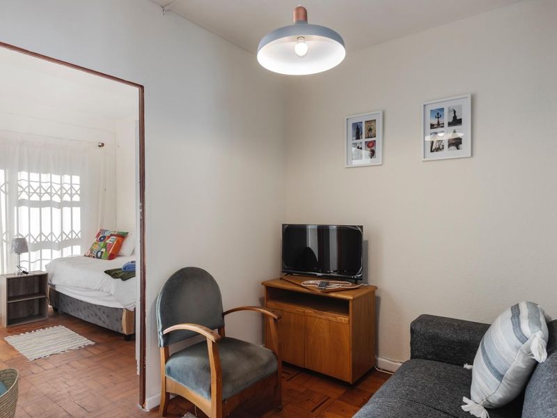 A cozy living area featuring classic parquet flooring and a pendant light, with an open doorway leading into an adjacent bedroom.
