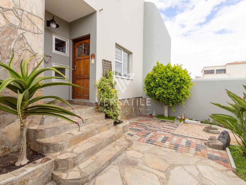 A well-maintained front entrance featuring stone-clad steps, a timber door, and a paved courtyard area.
