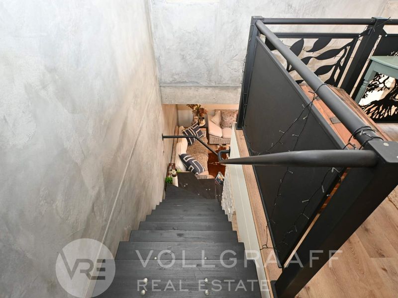 A modern staircase featuring dark timber treads, a sleek metal balustrade, and industrial-style concrete wall finishes, overlooking the lower living area.