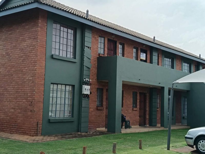 Exterior view of a two-story face brick apartment building featuring a balcony and tiled roof, with some minor damage to the facade cladding.