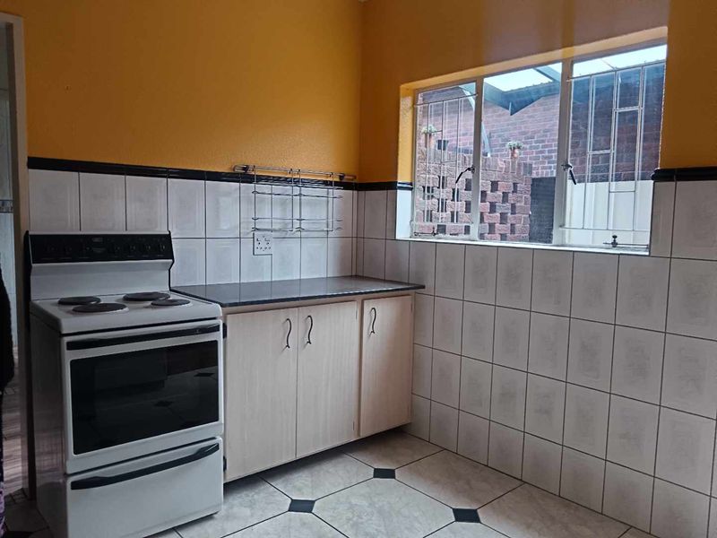 A functional kitchen featuring built-in cabinetry, a freestanding stove, tiled splashbacks, and security bars on the window.
