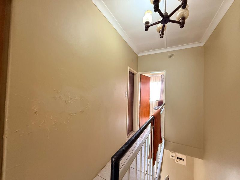 A hallway area featuring a staircase with a metal railing, tiled flooring, and a ceiling light fixture, showing signs of wall surface wear.