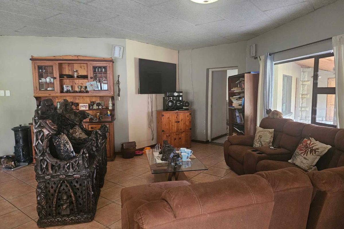 A living room featuring tiled flooring, a ceiling with acoustic tiles, and large windows providing natural light and access to the patio area.