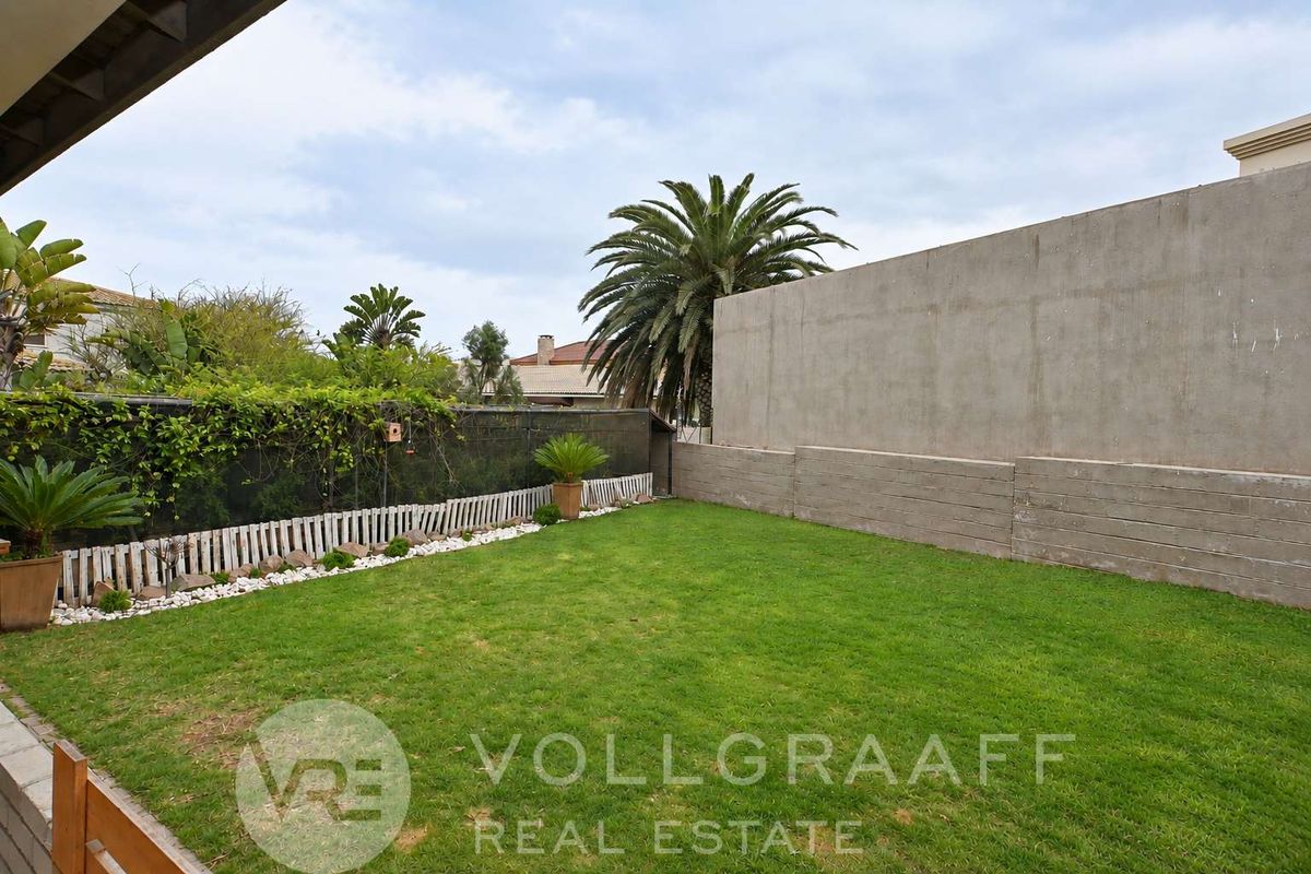 A private rear garden featuring a well-maintained lawn, bordered by a concrete boundary wall and mesh fencing with established greenery.