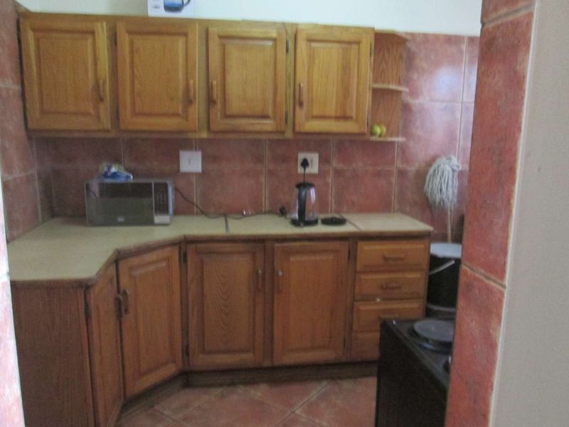 A dated kitchen featuring wooden cabinetry, laminate countertops, and tiled wall finishes, offering a functional layout with potential for modern updates.