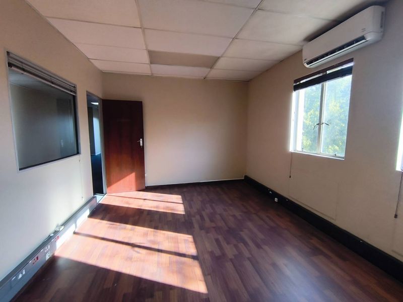 A vacant office space featuring laminate flooring, a suspended ceiling, an internal glass partition, and a wall-mounted air conditioning unit.