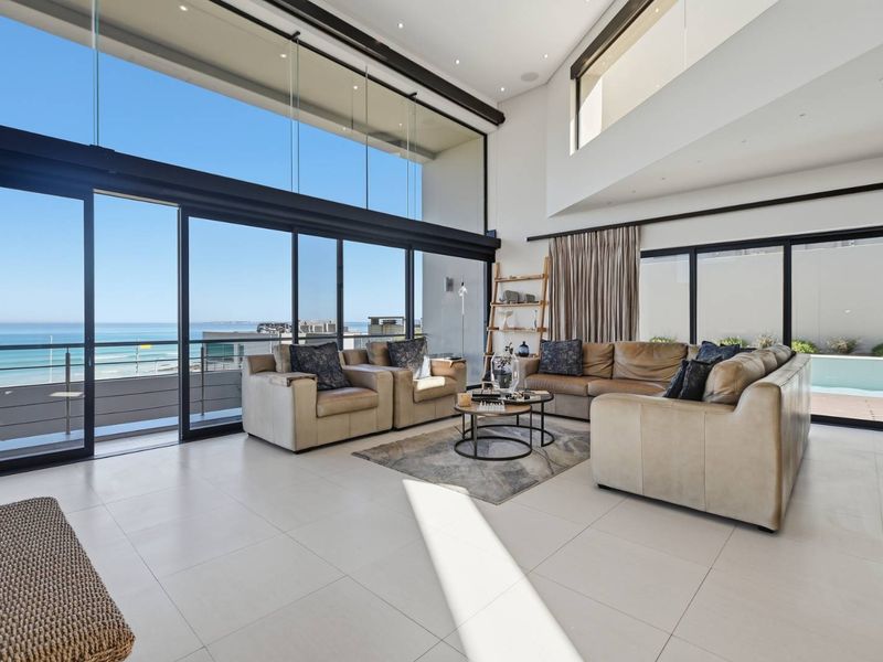 Spacious double-volume living area featuring expansive floor-to-ceiling glass doors that offer panoramic ocean views and seamless access to the outdoor patio.