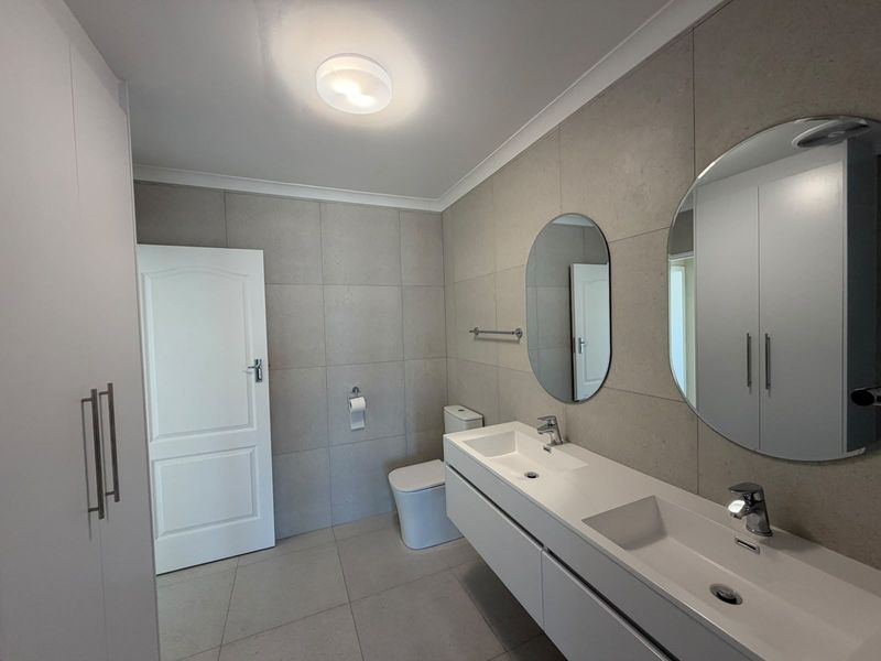 Modern bathroom featuring a sleek double vanity with dual basins, wall-mounted cabinetry, large circular mirrors, and neutral floor-to-ceiling tiling.