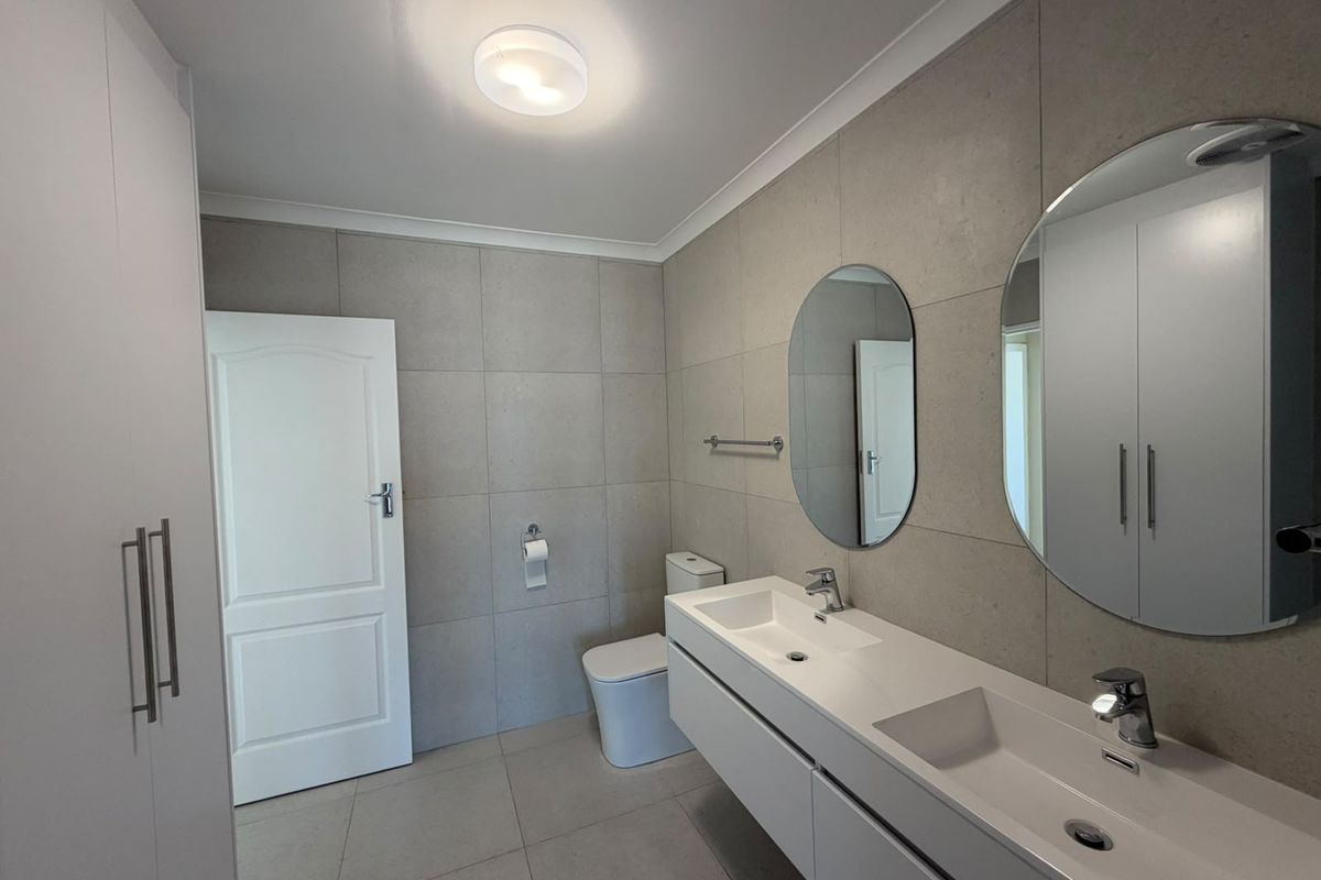 Modern bathroom featuring a sleek double vanity with dual basins, wall-mounted cabinetry, large circular mirrors, and neutral floor-to-ceiling tiling.