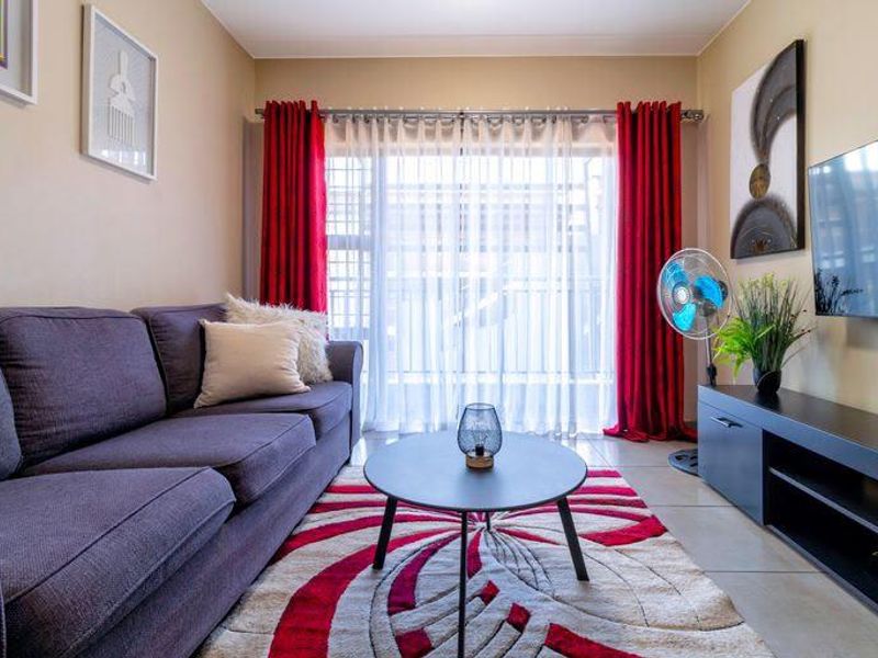 A well-maintained living room featuring tiled flooring and a large sliding glass door with curtain treatments, providing natural light to the space.