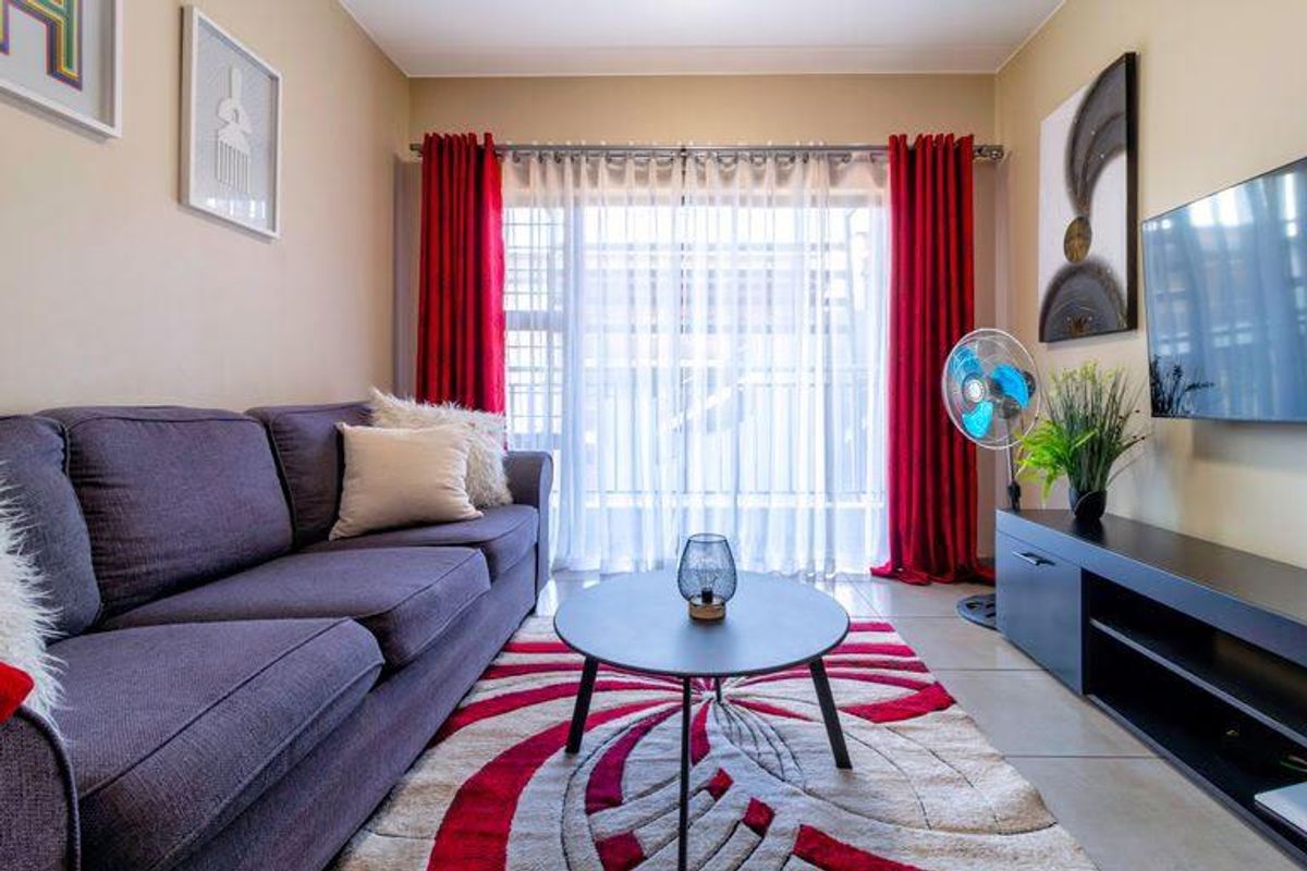 A well-maintained living room featuring tiled flooring and a large sliding glass door with curtain treatments, providing natural light to the space.