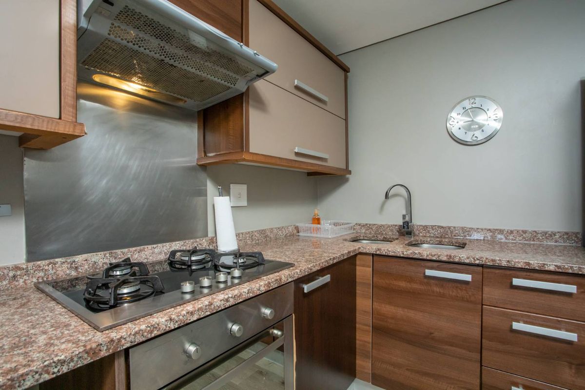 Compact kitchen featuring granite countertops, built-in gas hob, stainless steel oven, extractor fan, and double sink with modern cabinetry.