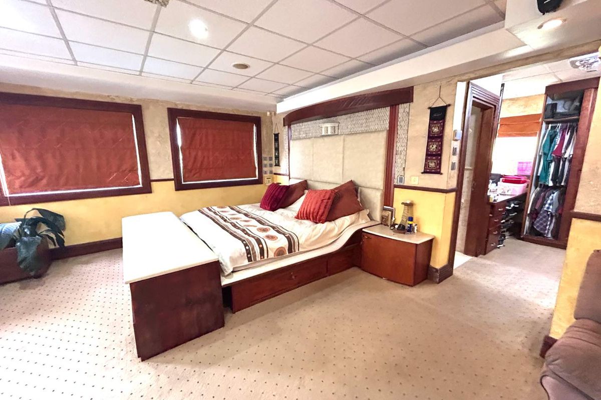 Spacious bedroom featuring a built-in headboard, integrated bedside cabinetry, and an adjoining walk-in closet area with neutral carpeting and recessed lighting.